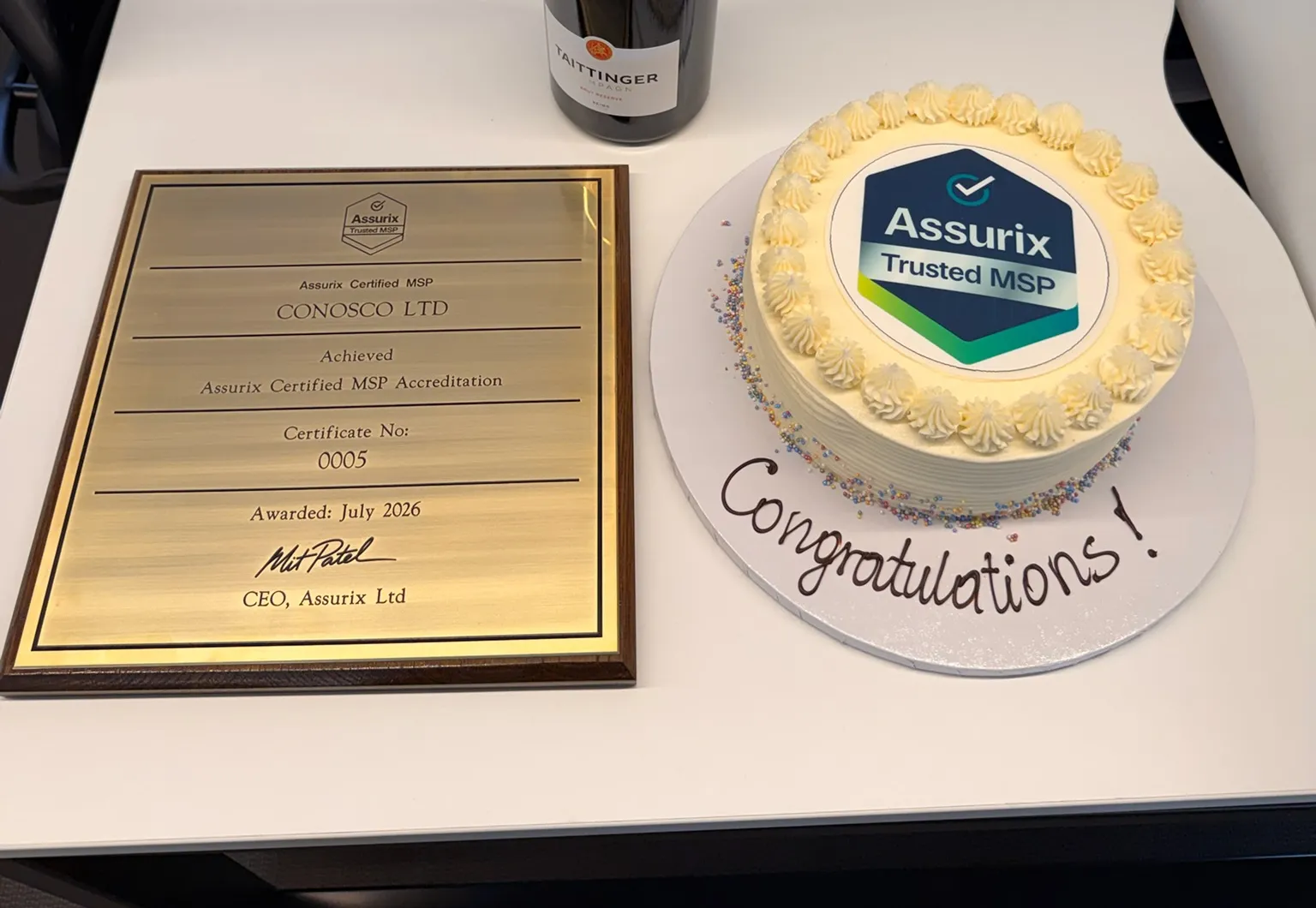 The Assurix Trusted MSP plaque for Conosco Ltd beside a cake iced with the Assurix Trusted MSP mark